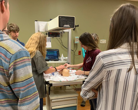 Students practicing medical skills on simulated, baby medical manikin.